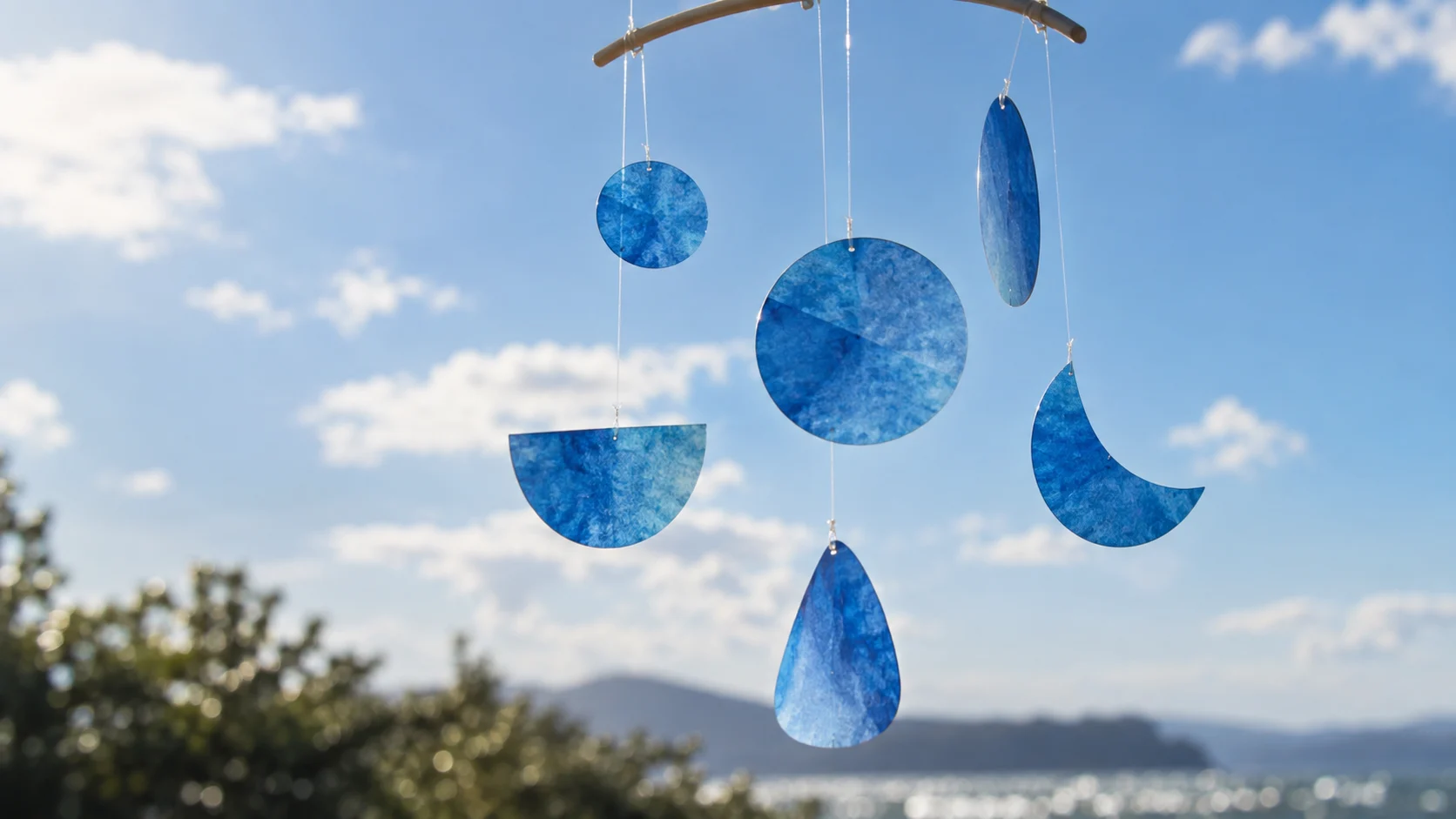 Abstract blue paper shapes hang in sunlight against a clear sky.