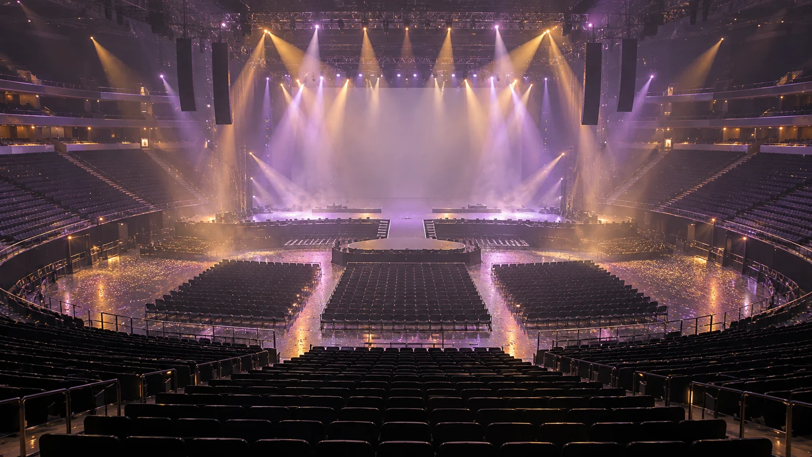 An empty pastel-lit concert stage viewed from the seats of a large arena.