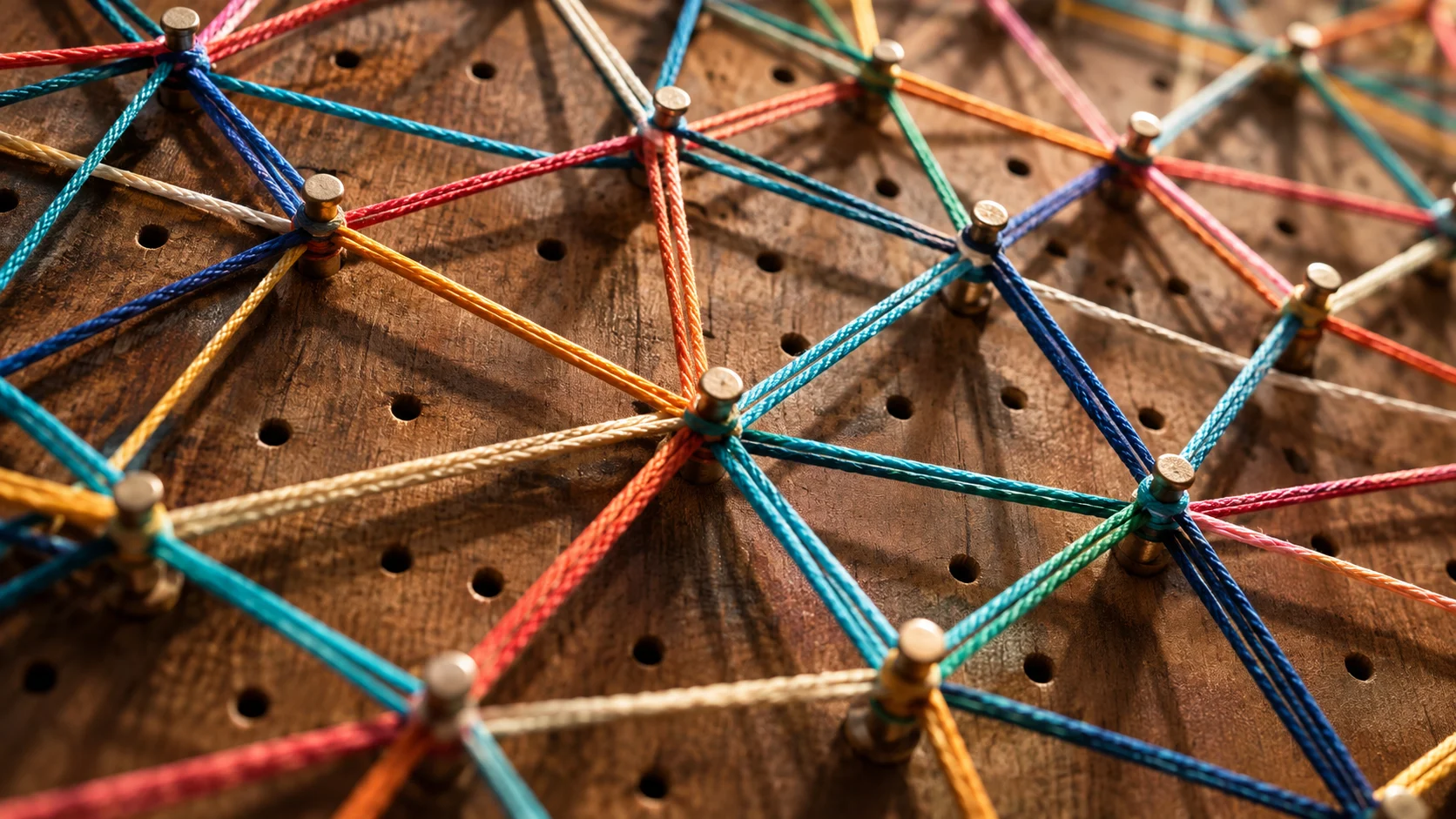 Bright cords cross and connect across a handcrafted wooden pegboard.